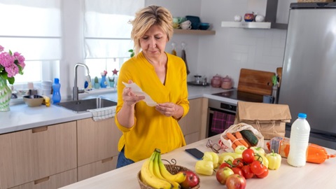 vrouw in de keuken met boodschappen voor zich kijkt naar haar kassaticket